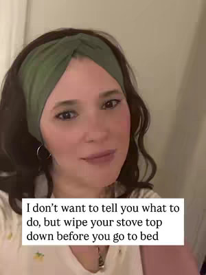 A woman with brown hair and a green headband is looking at the camera with a soft smile. Text at the bottom of the screen reads, "I don't want to tell you what to do, but wipe your stove top down before you go to bed."