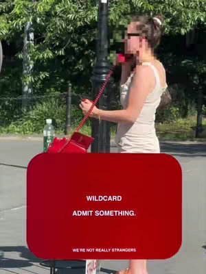 A woman in a cream-colored dress is shown from the waist up, standing by a lamp post in a park setting. She's holding a red telephone to her ear. A large red card with white text is overlaid on the bottom of the image. The background is filled with green trees and foliage.
