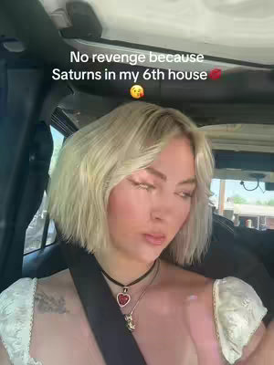 A woman in a car is the main subject of the cover image, with her upper body in focus. She has short, wavy blonde hair and is wearing a black necklace with a heart pendant. The car's interior and a glimpse of the outside world are visible in the background.