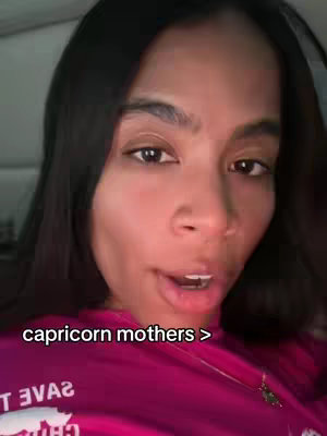 The cover image is a selfie-style shot of a woman with dark hair and fair skin filling most of the frame. Her expression is open-mouthed, as though she's speaking, and her eyes are directed toward the viewer. She is wearing a pink top partially visible at the bottom of the image, and the background is slightly blurred, suggesting an indoor setting. The overlaid text 'capricorn mothers >' is positioned at the bottom of the image.