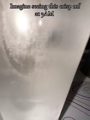 The image is a low-angle shot focusing on a transparent object, possibly a glass or a container filled with a cloudy liquid. The lighting has a bright source on the object's upper left side creating a hazy or misty effect within the image, and the background consists of a slightly darker, blurred pattern and a black element visible.