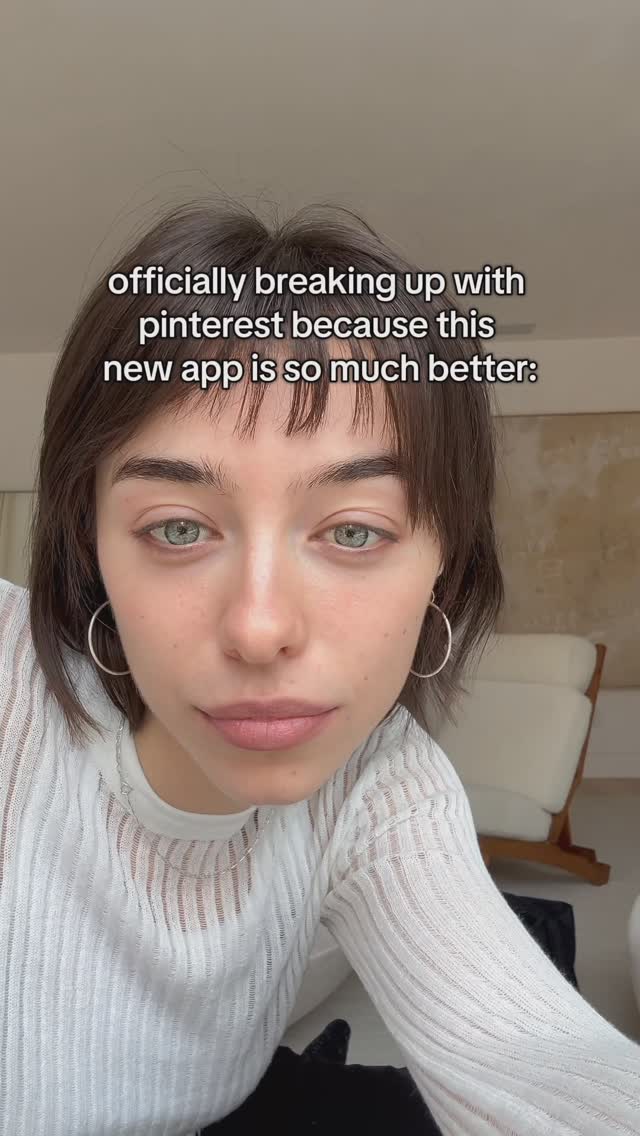 A close-up shot of a young woman with light skin, short dark hair, and green eyes. She is looking directly at the camera with a neutral expression. The text overlay reads, “officially breaking up with pinterest because this new app is so much better:”. The background is blurred, suggesting a domestic setting.