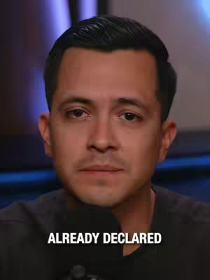 A man is centered in the frame, facing forward with a neutral expression. The background is slightly blurred, suggesting a studio setting with blue and white light accents. Text overlay at the bottom reads 'ALREADY DECLARED.'
