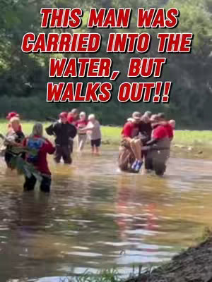 An outdoor scene with several people in shallow water. A man is being carried by others, with the text overlayed at the top.