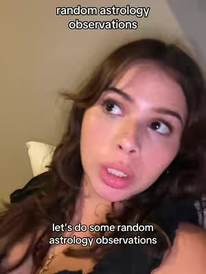 A woman looks up towards the right side of the frame with a slightly open mouth, as if she's about to speak. Her dark hair frames her face, and text overlays the image, with the top text stating 'random astrology observations' and the bottom text reading 'let's do some random astrology observations'. The background suggests a bedroom setting with dim lighting.