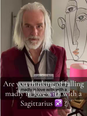 The cover image features a man with long gray hair and a white beard, wearing a burgundy blazer over a white shirt and a black tie. The background includes an abstract art piece and a pink lamp. Text overlay prompts viewers, referencing the Sagittarius zodiac sign.