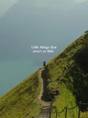 A scenic shot of a person walking up a stone path on a lush, green hillside. The path leads to the top, and the background shows a mix of blue sky and sea.