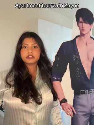 A woman stands in a room facing the camera beside a cardboard cutout of a male anime character. The text overlay reads 'Apartment tour with Zayne'.