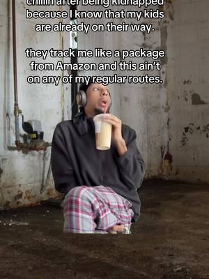 A man sits in a dimly lit, dirty basement, wearing headphones and a grey zip-up jacket over a black shirt, and plaid pajama pants. He holds a drink with a straw, looking upwards with an expression portraying surprise or concern. Behind him are pipes and concrete.