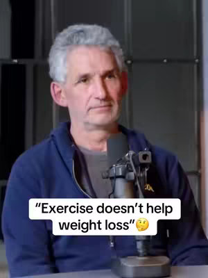 A middle-aged man with gray hair and a blue jacket is seated in front of a dark background. A microphone is positioned near his face, and a text overlay stating "Exercise doesn't help weight loss" is displayed on the image with a thinking emoji below the text.