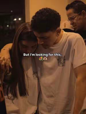 A warmly lit photo featuring two individuals embraced in a close hug, likely indoors. The focus is on a man and a woman, their faces close together, suggesting intimacy or a tender moment shared. Above them, a blurry background hints at a public setting or a casual social gathering. The overall mood is gentle and relational.