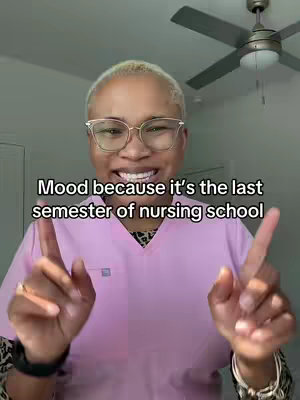 A woman with short, blonde hair and glasses smiles as she points two fingers up towards the camera, with a ceiling fan visible in the background. Text overlay says "Mood because it's the last semester of nursing school". She is wearing a pink scrub top.