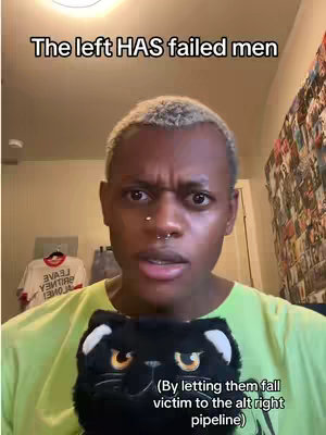 A person with short, light hair looks directly at the camera with a concerned expression. The person is wearing a light green shirt and holding a black plush cat. The background includes a white t-shirt with writing hanging on the wall and a cluttered, semi-visible wall. Text overlays are present at the top and bottom of the image.