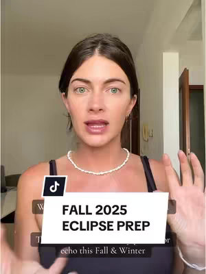 A woman with fair skin and green eyes is centered in the frame, looking directly at the viewer. She has dark, shoulder-length hair and is wearing a white beaded necklace and a black top. A TikTok logo is visible in the top-left corner, and a white rectangle with text overlay is placed in front of her, partially obscuring her body. The background is blurred, indicating an indoor setting.