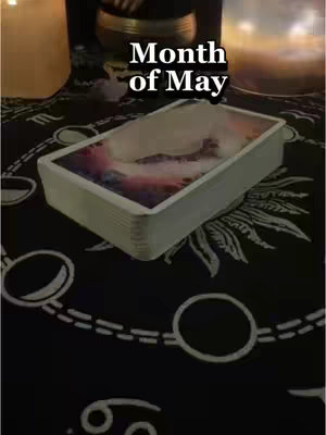A top-down shot showcases a black cloth adorned with white circular and crescent moon patterns. A deck of tarot cards is neatly stacked in the center. Above the deck lies the text overlayed over a candle lit background and another candle to the left. The overall composition is dimly lit with warm highlights.