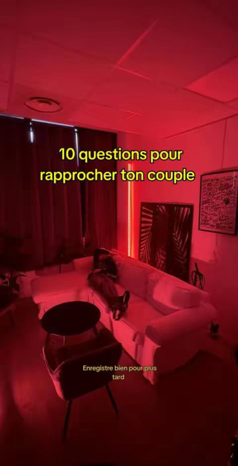The image shows a dimly lit room with a red hue. In the center, a white couch is visible, with a person lying on it. In the background, there is a framed picture, and to the right, there is a decorative panel with a leaflike design. At the bottom of the image reads: 'Enregistre bien pour plus tard'.