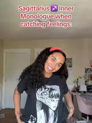 A woman with dark curly hair and a red headband smiles directly at the camera, wearing a black t-shirt with a graphic design. The background is a room with tan walls and a closed white door. Text overlays the image in a pinkish-red color.