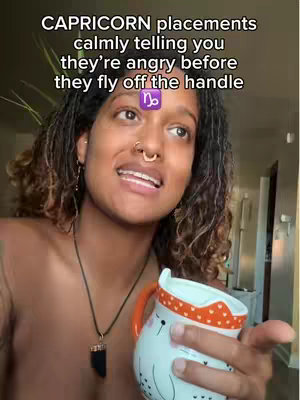 A woman with brown skin and curly hair is the central figure, seen from the chest up. She is positioned slightly off-center, looking toward the viewer, with a warm, inviting expression. She has several facial piercings and is holding a white cup with an orange handle and heart-shaped patterns. The background is out of focus but appears to be an indoor setting, possibly a home. The hook text is overlaid at the top, and a Capricorn symbol is overlaid on her forehead.