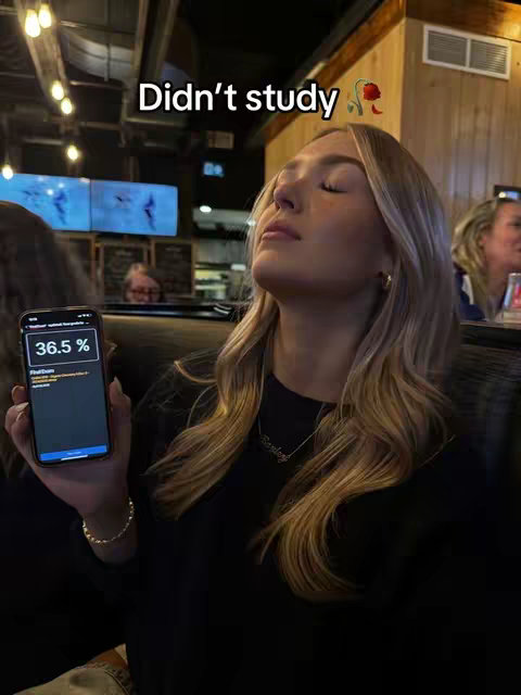 A woman with long blonde hair is seated, holding a phone displaying a study app. The overlay text reads 'Didn't study'. The background is a dimly lit restaurant setting.