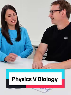 The cover image captures two individuals seated at a table. A woman on the left is wearing a light blue long-sleeved shirt and is holding a piece of paper, while a man on the right, wearing glasses, is smiling and looking towards the woman. A banner with white text 'Physics V Biology' which is placed over a stack of paper, at the bottom of the image.