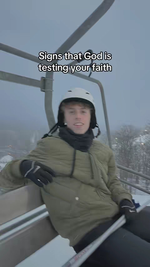 A young man wearing a ski helmet, jacket, and gloves is on a ski lift, set against a snowy, overcast background. Text overlayed on the image reads "Signs that God is testing your faith."
