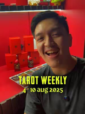 A vertical shot featuring a man smiling widely directly at the camera. He has short dark hair and is wearing a dark shirt. In the background, a bright red wall is visible, along with some red boxes. The text 'TAROT WEEKLY' is overlaid on the bottom of the image in a yellow font, followed by '4-10 aug 2025'.