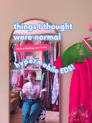 A woman sits in front of a mirror, the reflection showing a closet filled with clothes. Text overlays highlight the topic of the video – things she thought were normal, relating to hypermobile Ehlers-Danlos Syndrome. The overall composition includes a sense of discovery and personal reflection.