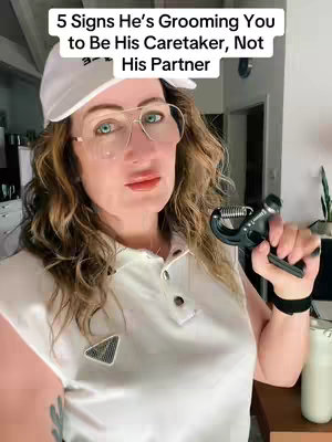 A woman in a white polo shirt and a white cap, wearing glasses, looks directly at the camera. She is holding a hand grip strengthener. Text overlayed at the top says, "5 Signs He's Grooming You to Be His Caretaker, Not His Partner".
