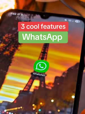 A phone screen displays the WhatsApp app icon over a background image of Paris and the Eiffel Tower at sunset. A rectangular section at the top contains text, seemingly overlaid on the phone's interface, in red and green blocks. Part of a hand is visible in the lower part of the frame, holding the phone.