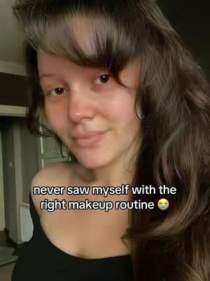 A selfie-style shot featuring a woman's upper body. She has long, wavy brown hair with blonde highlights framing her face. She's looking directly at the camera with a slight smile, and the lighting appears soft and natural. The hook text 'never saw myself with the right makeup routine' is displayed in a lower area of the image, accompanied by a crying emoji.