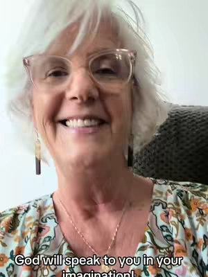 The image is a close-up of a smiling older woman with white hair and glasses. She is wearing a blouse with a floral pattern and simple earrings. Text at the bottom of the image says 'God will speak to you in your imagination!'