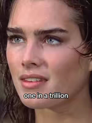 A close-up of Brooke Shields' face is displayed, with her blue eyes and light skin prominently featured. She appears to be gazing slightly to the side, her expression a mix of thought and slight emotion. Overlaid on the image is the text "one in a trillion". The overall composition is simple, focusing on the subject's face against a blurred background.