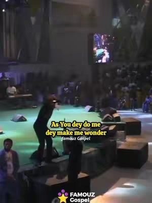 The image shows a live performance setting. A man in dark clothing is on stage, mid-performance, with a microphone, silhouetted against stage lighting. A large screen displays visuals behind him. The audience and stage elements create a sense of movement and energy.