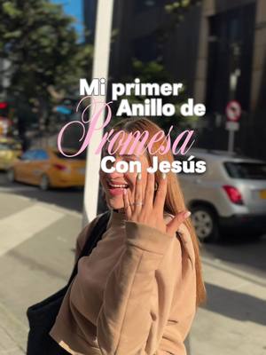 A woman with long hair smiles, holding up a hand to display a ring. Text overlayed on the image reads 'Mi primer Anillo de Promesa Con Jesús'. The background shows a city street with buildings and a car.