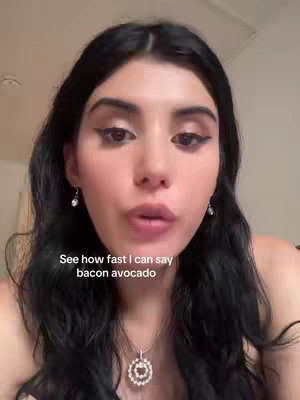 A selfie-style video cover with a young woman in the center, framed from the chest up. She has dark hair and is looking directly at the camera. She’s wearing a simple necklace. Text overlayed on the image says, 'See how fast I can say bacon avocado.' The background is out of focus. The lighting is soft, and the overall composition is simple, focusing on the woman's face.