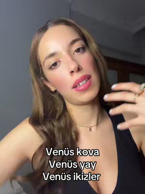 The cover image shows a woman in a medium close-up from the chest up, with lightly tanned skin, wearing pink lip gloss, a medium-sized necklace with a small pendant, and a black top. She has long, light brown hair. The background consists of a light gray color. Overlayed at the bottom are three lines of white text.