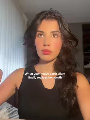 The image is a selfie-style shot of a young woman with dark hair and a black top. The background appears to be a neutral, indoor setting, likely a home or apartment. The woman is looking at the camera with a neutral expression. Text is overlaid at the bottom of the image.