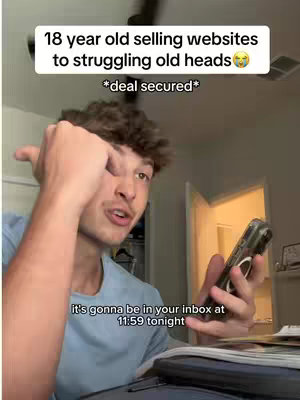 A young man in a light blue shirt is shown holding a phone in his right hand and touching his face. Overlay text at the top of the frame reads, '18 year old selling websites to struggling old heads' and has text beneath it also. There's text at the bottom, too. The room has a ceiling fan