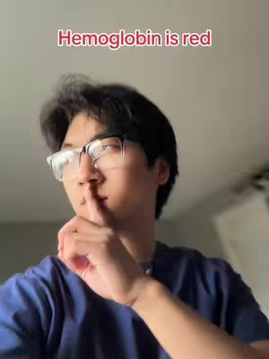 A medium shot shows a young man with dark hair wearing glasses and blue scrubs.  He is covering his mouth with his finger, as if to shush the viewer.  Above him, the text "Hemoglobin is red" appears in a red font.