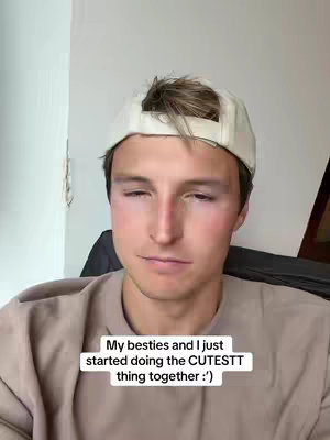 A young man with short, light brown hair, wearing a white baseball cap turned slightly to the side. He wears a light brown, crew-neck shirt. The text overlay states, "My besties and I just started doing the CUTESTT thing together :’)"