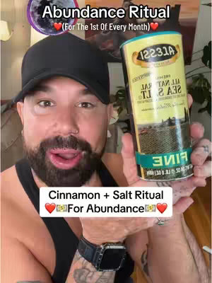A man in a black cap and tank top holds a can of sea salt, with text overlays indicating an abundance ritual. The background is blurred, focusing attention on the man and the product.