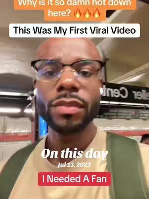 A selfie-style video cover image showing a Black man in glasses and a light colored t-shirt, in a subway setting. Text overlays include a question: "Why is it so damn hot down here?" above the title "This Was My First Viral Video" in a white box. Additional text indicates the date "Jul 13, 2023" and states "I Needed A Fan".