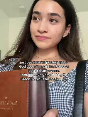A young woman with long dark hair and a plaid top poses for a selfie, holding a brown book and appearing to look upward thoughtfully. Text overlaid on the image includes a quote about sharing her faith and leaning on God for strength.