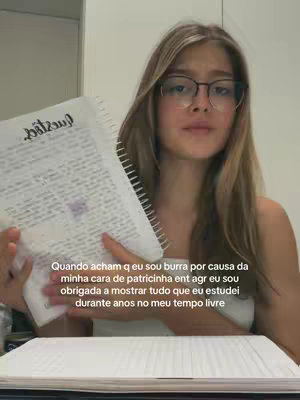 A young woman with long blonde hair and glasses is holding an open notebook, likely a school one, and looking towards the camera. Text is overlaid on the image, and she's wearing simple clothing, giving a relatable aesthetic.
