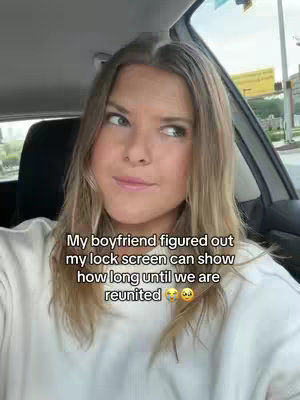 A woman is seated inside a car, looking slightly off-camera with a small smile. Text over the image reads about her phone lockscreen showing how long until she and her boyfriend are reunited.