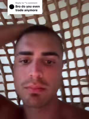 A close-up shot of a man's face, partially obscured by a latticework background. He has short, dark hair, a trimmed beard, and a neutral expression. The background is a woven pattern of light brown material.