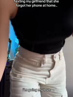 The shot captures a person from the mid-torso down, dressed in a black tank top and off-white pants. The background is blurred, but hints of a room are visible, suggesting an indoor setting.