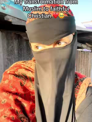 A person wearing a black niqab with only their eyes visible, against an out-of-focus backdrop. The person is wearing a bright red patterned top and there is an overlay of text at the top.