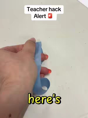 A hand holding a blue balloon, with text overlays stating 'Teacher hack Alert' and 'here's'. The video appears to be filmed on a white surface.