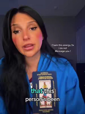 A woman holding a tarot card, with overlaid text stating 'that this person's been...' The woman has dark hair and is wearing a blue jacket. Background has soft, diffused lighting.